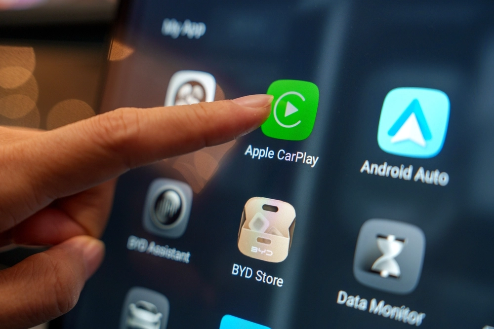 Close-up of a hand tapping the Apple CarPlay app on the digital display inside a BYD electric car.