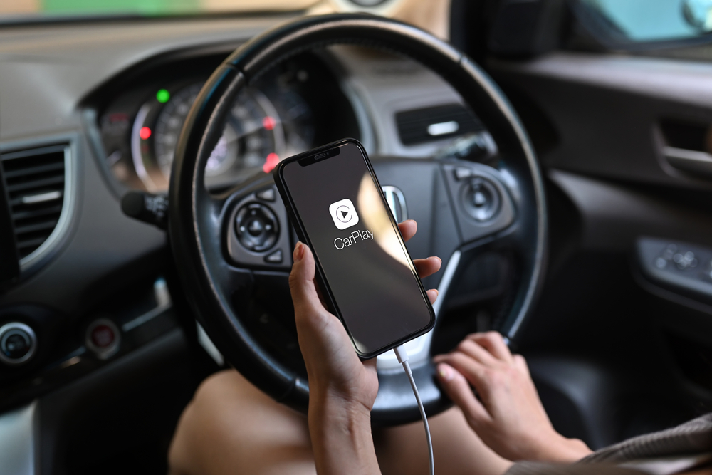 Woman holding iPhone 12 Pro max with car play in the screen multimedia system auto